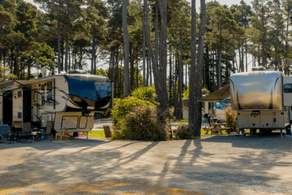 two 5th wheel trailers parked side by side on a camping lot 