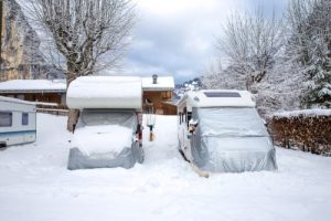 Two RVs with covers over them sitting in deep snow.